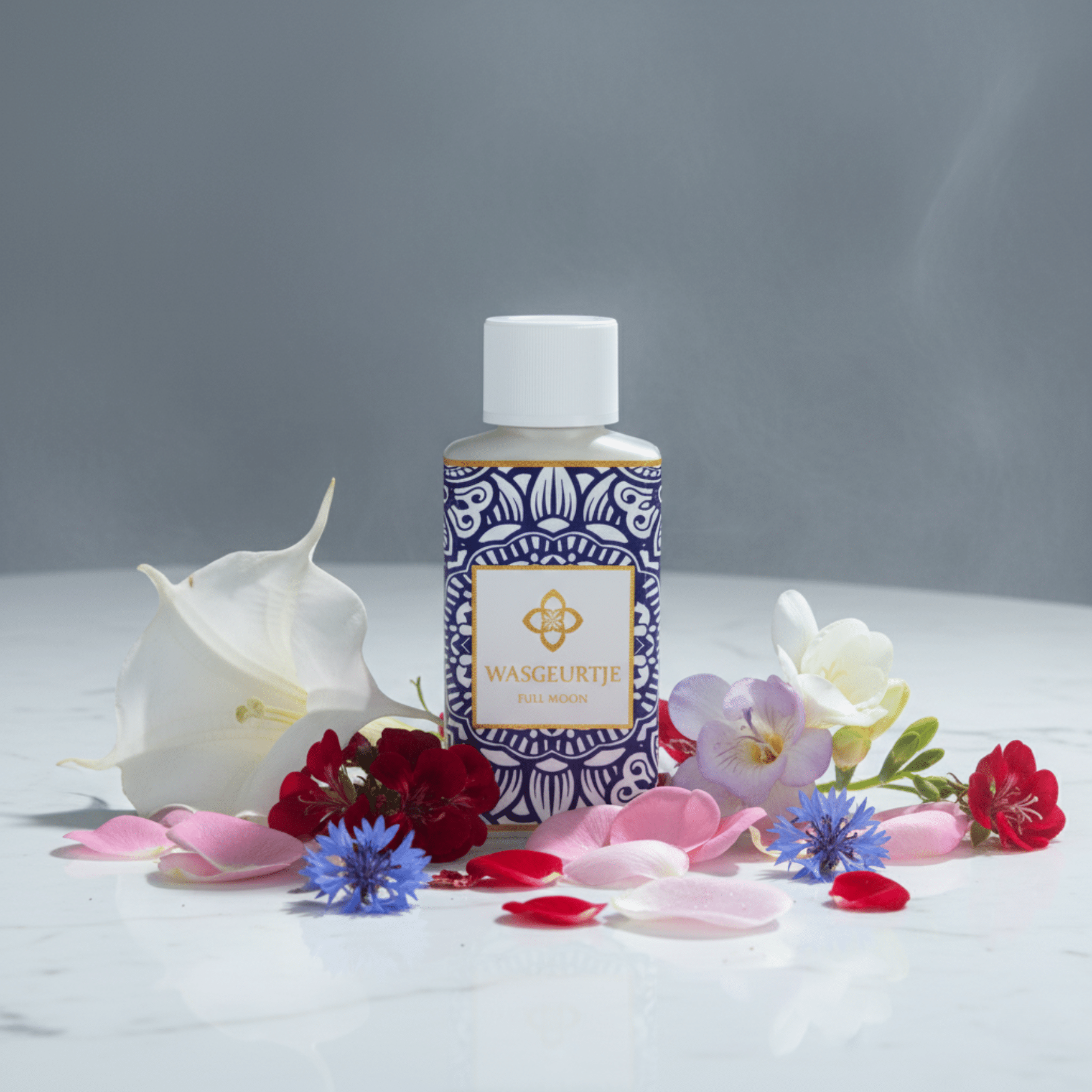 Flesje Wasgeurtje Full Moon wasparfum tussen kleurrijke bloembladen in rood, roze, wit en blauw op een marmeren oppervlak.