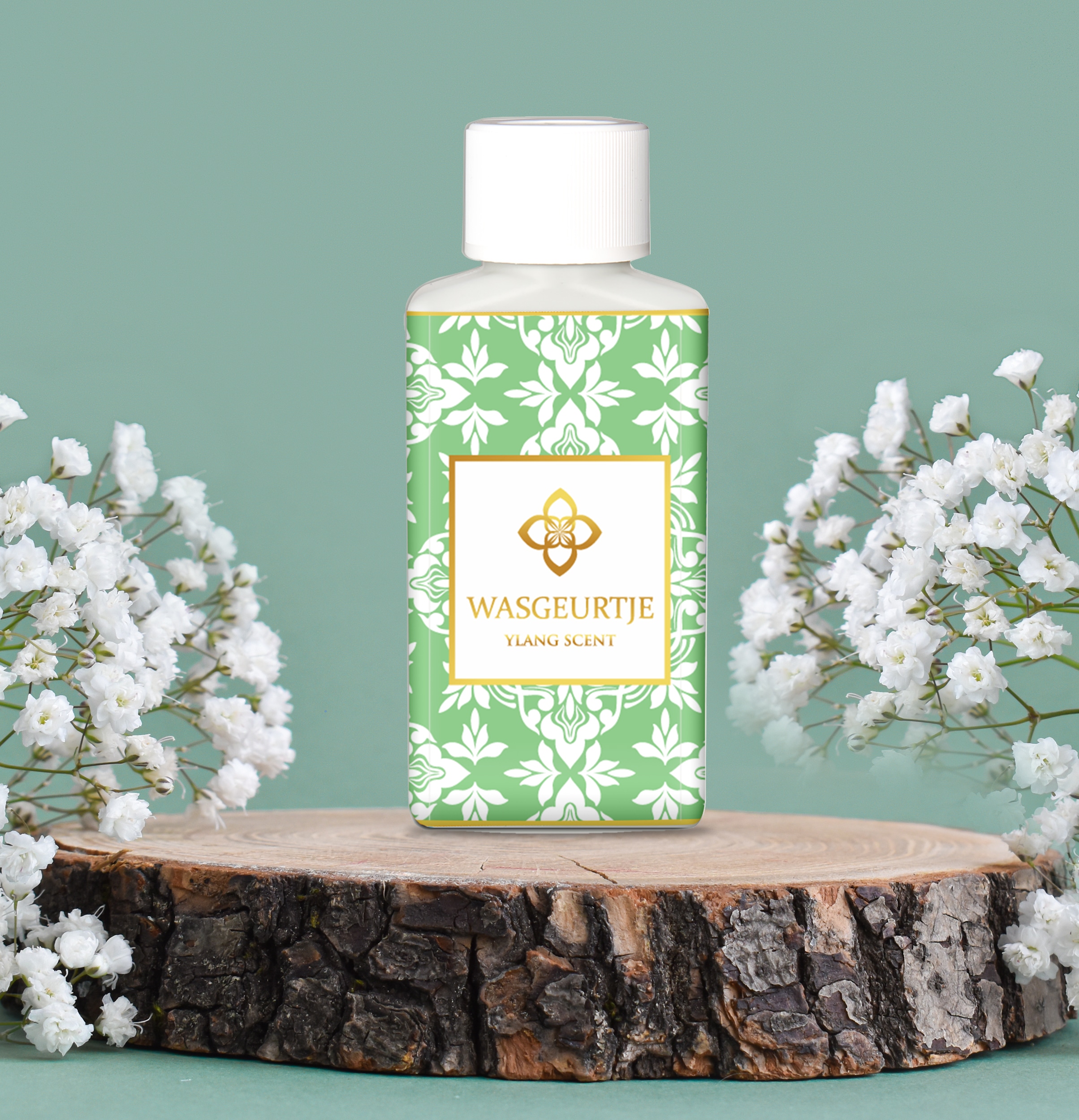 Wasgeurtje Ylang Scent wasmiddel met een groen en wit floraal patroon, naast witte bloesems op een houten schijf.